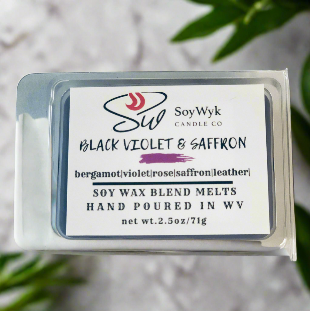 White Soy wax melt in 2.5 oz clear package labeled “Black Violet & Saffron” on a white ceramic counter in kitchen surrounded by green plants. Featured fragrant notes are bergamot, violet, rose, saffron, leather. Hand- poured in WV by SoyWyk Candle Co. 