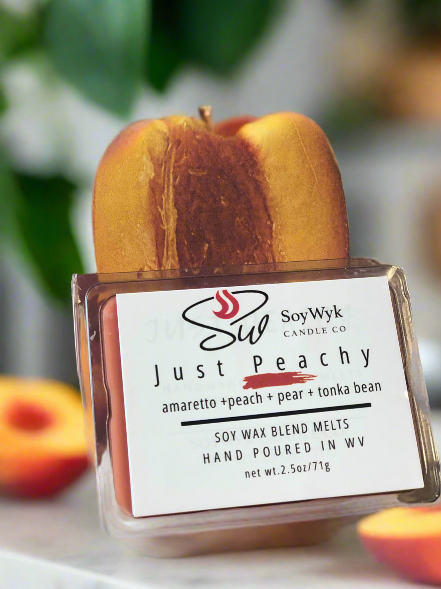 White Soy Wax Melt in a 2.5 oz clear package. Wax Melt on white kitchen countertop  against a large peach cut in half behind the wax melt with other peach halves on the counter. Labeled as “Just Peachy”. 
Featured fragrant notes are amaretto, peach, pear, tonka bean. 
Hand-poured in WV by SoyWyk Candle Co. 