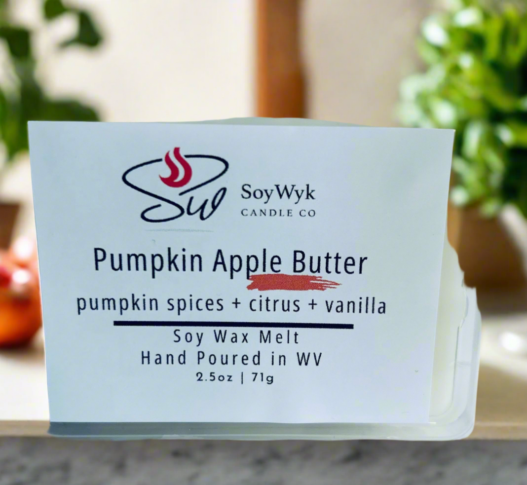 White Soy Wax Melt 2.5 oz in a clear package labeled “ Pumpkin Apple Butter” Featured fragrant notes are pumpkin spices, citrus, vanilla pictured in a modern white kitchen on a white ceramic counter with apples and house plants surrounding the melt. Hand-poured in WV by SoyWyk Candle Co. 