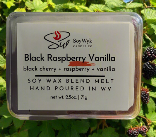White Soy wax melt in 2.5 oz clear package labeled “Black Raspberry Vanilla” positioned in the middle of a blackberry bush.Featured  fragrant notes are black cherry, raspberry, vanilla. Hand-poured by  
Soywyk Candle Co in WV.