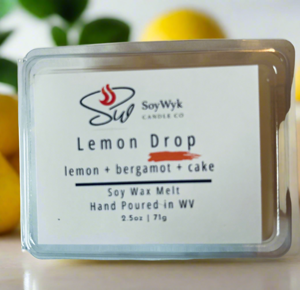 White Soy wax melt in a 2.5 oz clear package labeled “Lemon Drop “ on a white countertop surrounded by lemons and greenery. Featured fragrant notes are lemon, bergamot, cake. 
Handpoured in WV by SoyWyk Candle Co. 