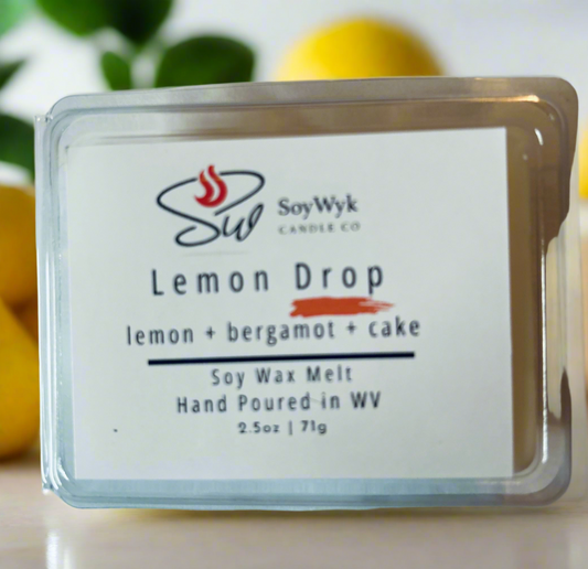 White Soy wax melt in a 2.5 oz clear package labeled “Lemon Drop “ on a white countertop surrounded by lemons and greenery. Featured fragrant notes are lemon, bergamot, cake. 
Handpoured in WV by SoyWyk Candle Co. 