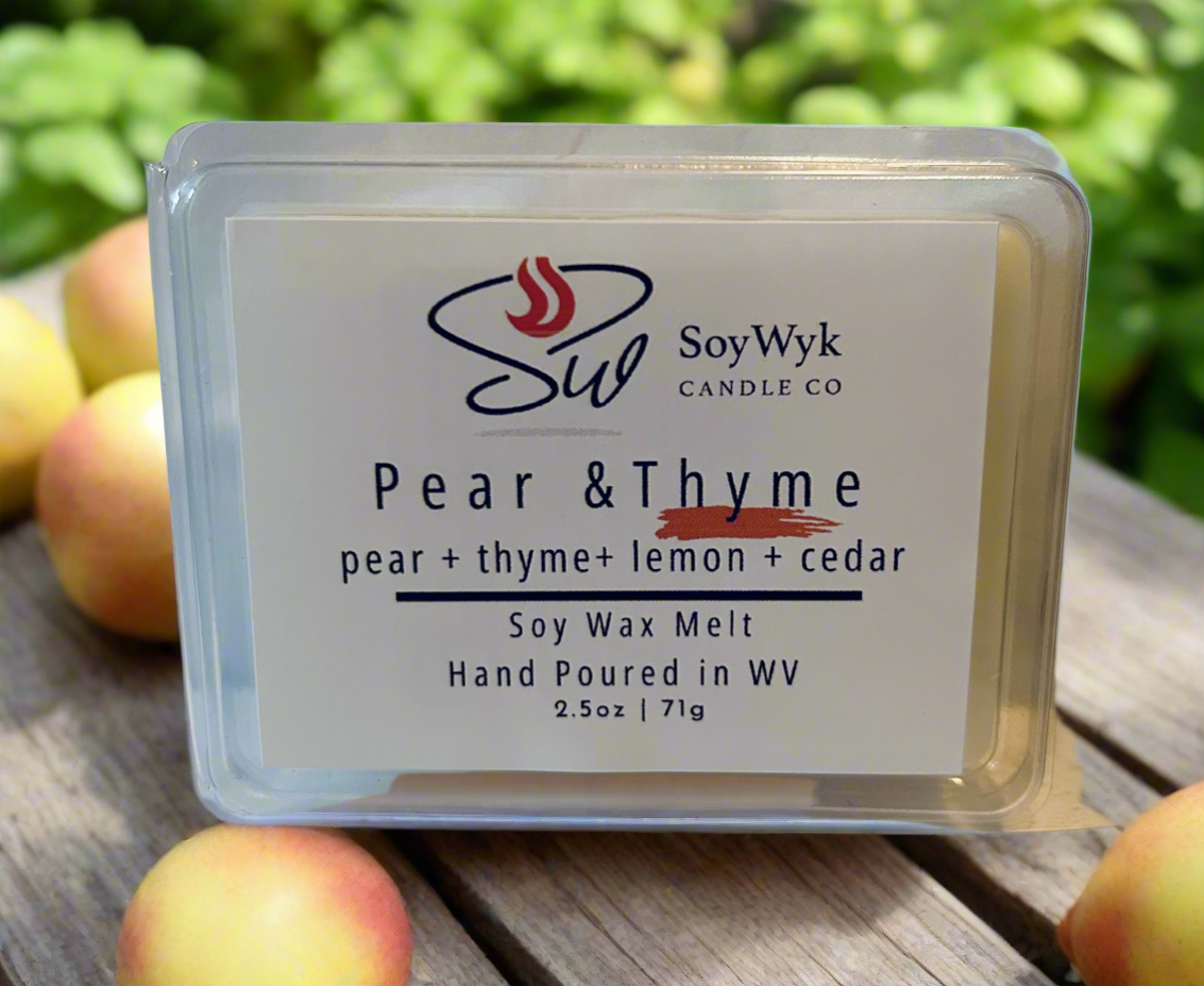White Soy wax melt packaged 2.5 oz clear package labeled “Pear & Thyme” Featured fragrant notes are pear, thyme, lemon, cedar. Sitting in a wood bench surrounded by pears and thyme in outdoor area. -Handpoured in WV by SoyWyk Candle Co. 