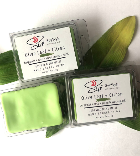 White Soy Wax Melt in a 2.5 oz clear package.  The wax melt is in the center of a white background with green leaves scattered under them. Labeled as “Olive Leaf & Citron”. 
Featured fragrant notes are bergamot, rose, green leaves, musk 
Hand-poured in WV by SoyWyk Candle Co. 