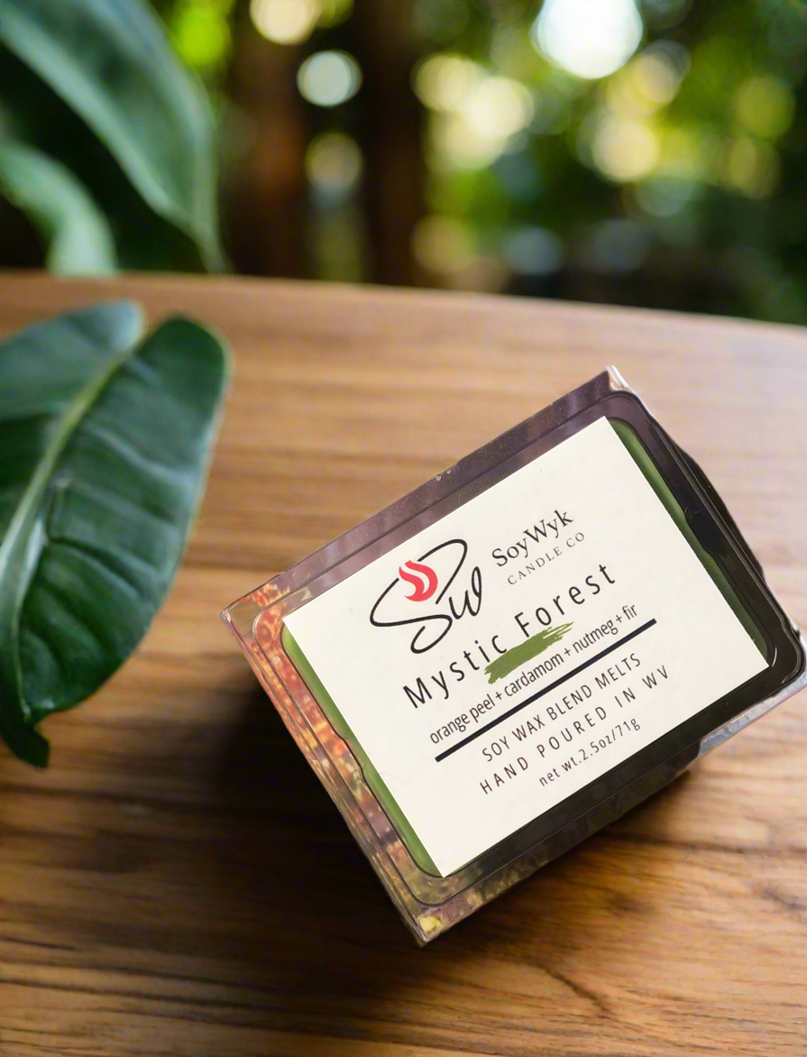 White Soy Wax Melt in a 2.5 oz clear package.  The wax melt is outside in the forest on a wood table surrounded by forest vegetation. Labeled as “Mystic Forest “. 
Featured fragrant notes are orange, cardamom, peppercorn, ginger, cinnamon, Fir
Hand-poured in WV by SoyWyk Candle Co. 