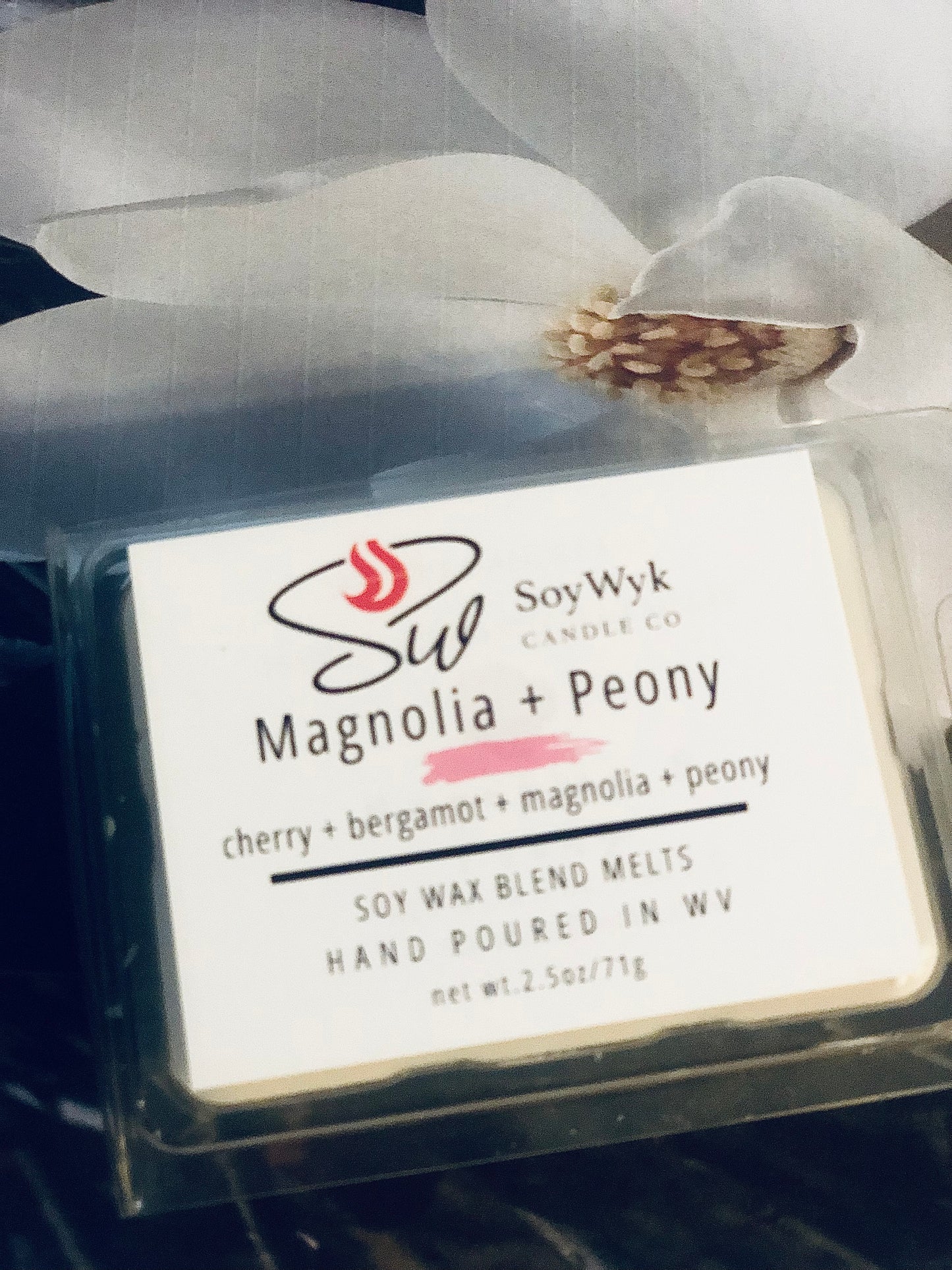 White Soy Wax Melt in a 2.5 oz clear package. A large white magnolia flower with a yellow center is behind the wax melt. the Labeled as “Magnolia & Peony”. 
Featured fragrant notes are cherry, bergamot, magnolia, peony. 
Hand-poured in WV by SoyWyk Candle Co. 
