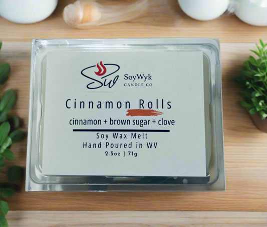 White Soy Wax Melt 2.5 oz in a clear package on a modern kitchen counter with plants. Labeled  “Cinnamon Rolls”. Featured fragrant notes are cinnamon, brown sugar, 
Clove. Hand- poured in wv by SoyWyk Candle Co. 