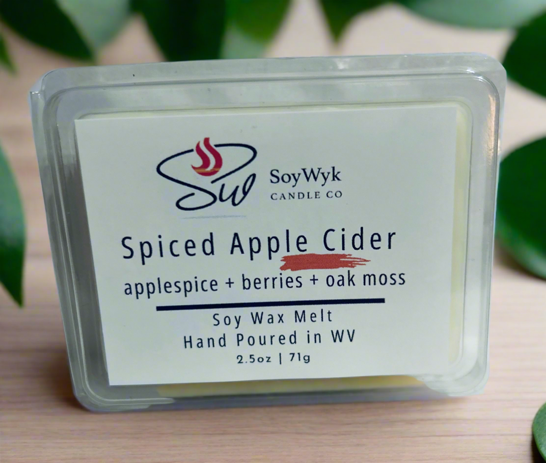 White Soy wax melt in 2.5 oz clear package labeled “Spiced Apple Cider” on a wood counter in kitchen surrounded by green plants. Featured fragrant notes are  Apple spice , berries, oak moss . Hand- poured in WV by SoyWyk Candle Co. 