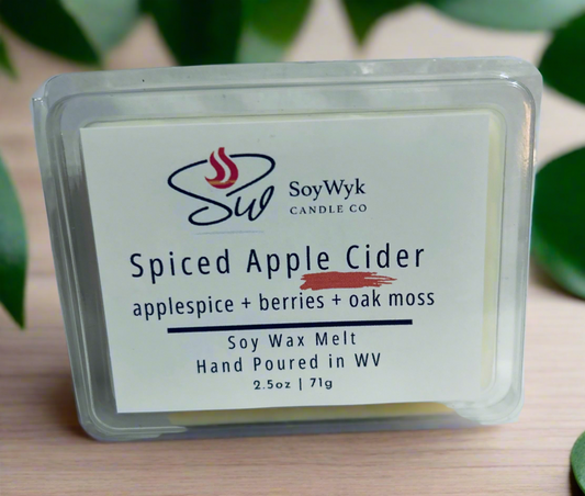 White Soy wax melt in 2.5 oz clear package labeled “Spiced Apple Cider” on a wood counter in kitchen surrounded by green plants. Featured fragrant notes are  Apple spice , berries, oak moss . Hand- poured in WV by SoyWyk Candle Co. 