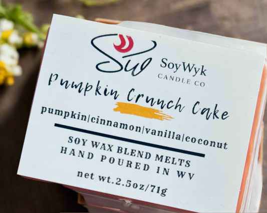 White Soy Wax Melt 2.5 oz packaged in a clear container labeled “Pumpkin Crunch Cake “ Featured fragrant notes are pumpkin, cinnamon, vanilla, coconut. In a wood countertop with flowers in background. 
Hand-poured in WV by SoyWyk Candle Co. 