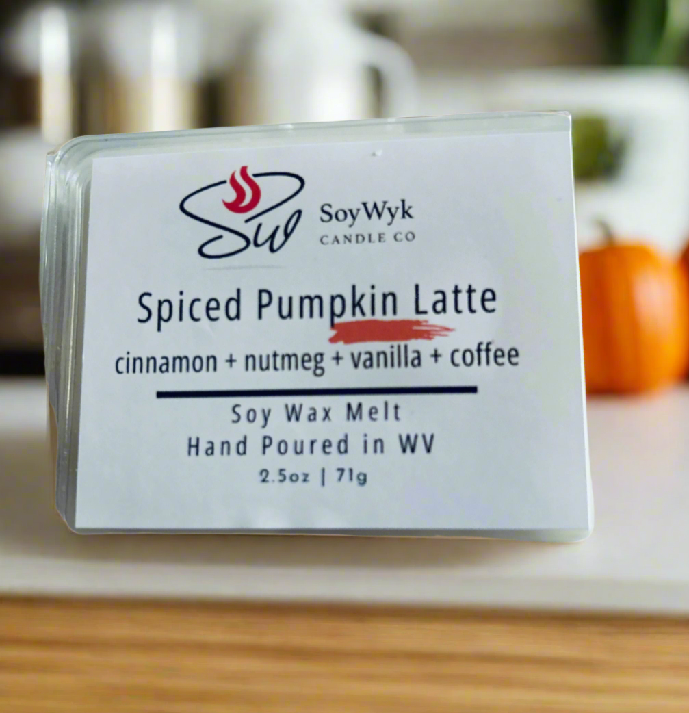 White Soy Candle  melt packaged in a clear package labeled “ Spiced Pumpkin Latte” 
Featured fragrant notes are cinnamon, nutmeg, vanilla, coffee in a modern kitchen on a wood countertop with pumpkins and kitchen furniture in background. Hand-poured in WV by SoyWyk Candle Co. 