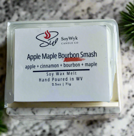 White Soy wax melt in 2.5 oz clear package labeled “Apple Maple Bourbon Smash” on a ceramic white and black counter in kitchen surrounded by green plne.  Featured fragrant notes are  apple, cinnamon, bourbon, maple. 
Hand- poured in WV by SoyWyk Candle Co.
